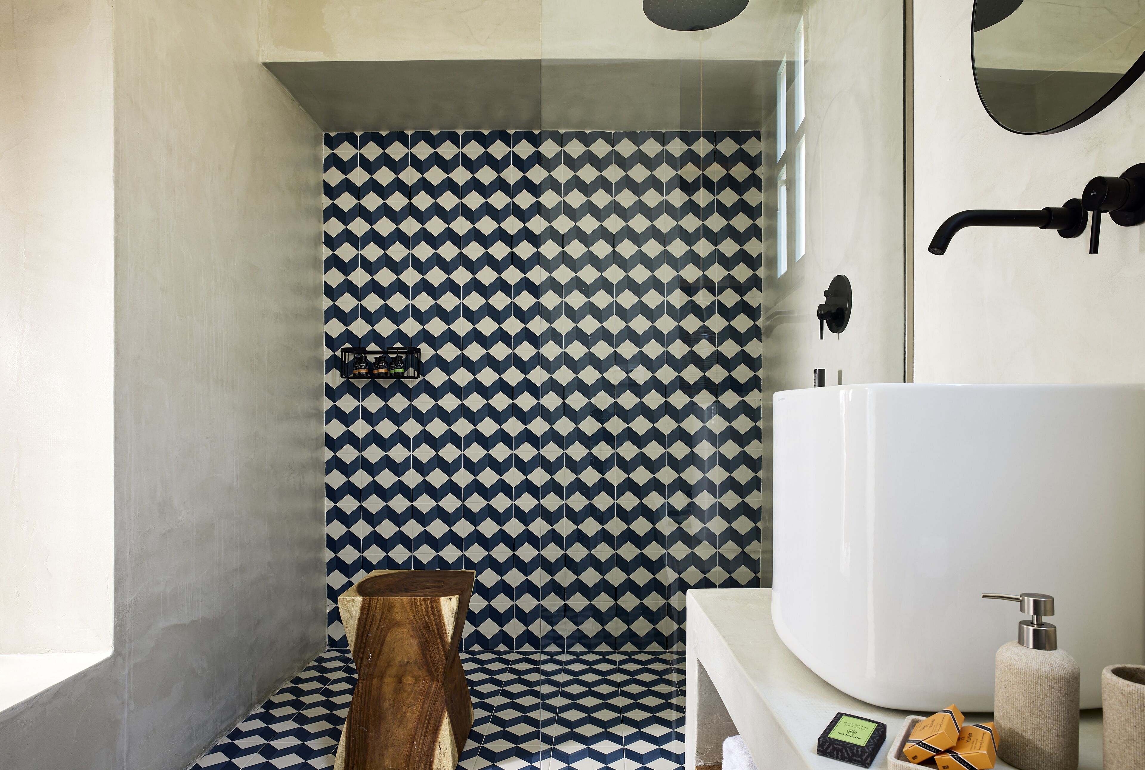 Un baño moderno con un patrón geométrico de azulejos, una bañera grande y un taburete de madera.