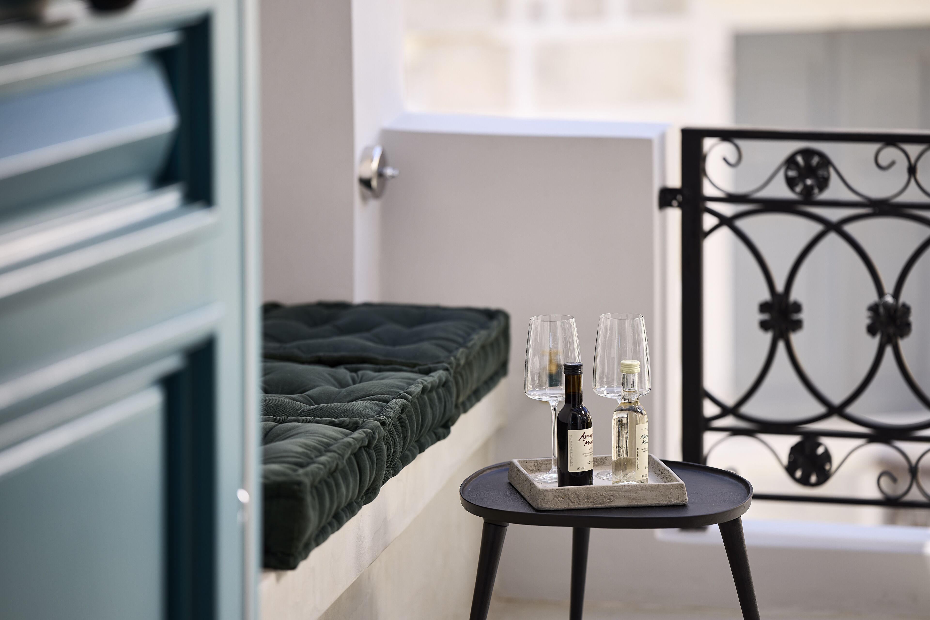 A bedroom with a dark green bed, a small table with wine glasses and bottles, and a decorative metal gate in the background.