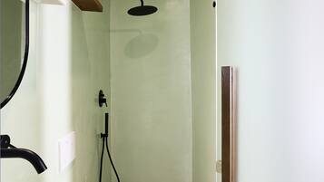 A bathroom with a white bathtub, a shower with a black hose, a wooden shelf with toiletries, and a patterned floor.