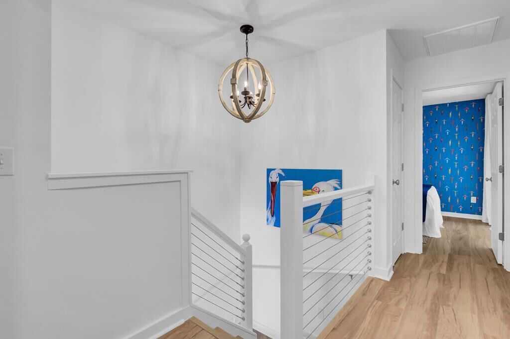 A hallway with white walls, a wooden floor, and a chandelier. There is a blue door with a pattern and a white towel hanging on the door frame.
