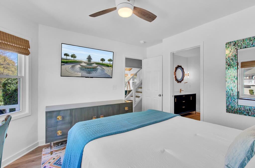 A bedroom with a bed, a TV mounted on the wall, a ceiling fan, and a view of a staircase.