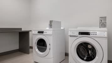 Two front-loading Whirlpool washers in a modern laundry room with a grey countertop and a grey wall.
