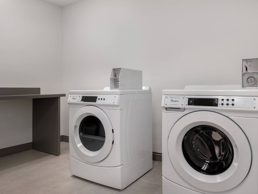 Two front-loading Whirlpool washers in a modern laundry room with a grey countertop and a grey wall.