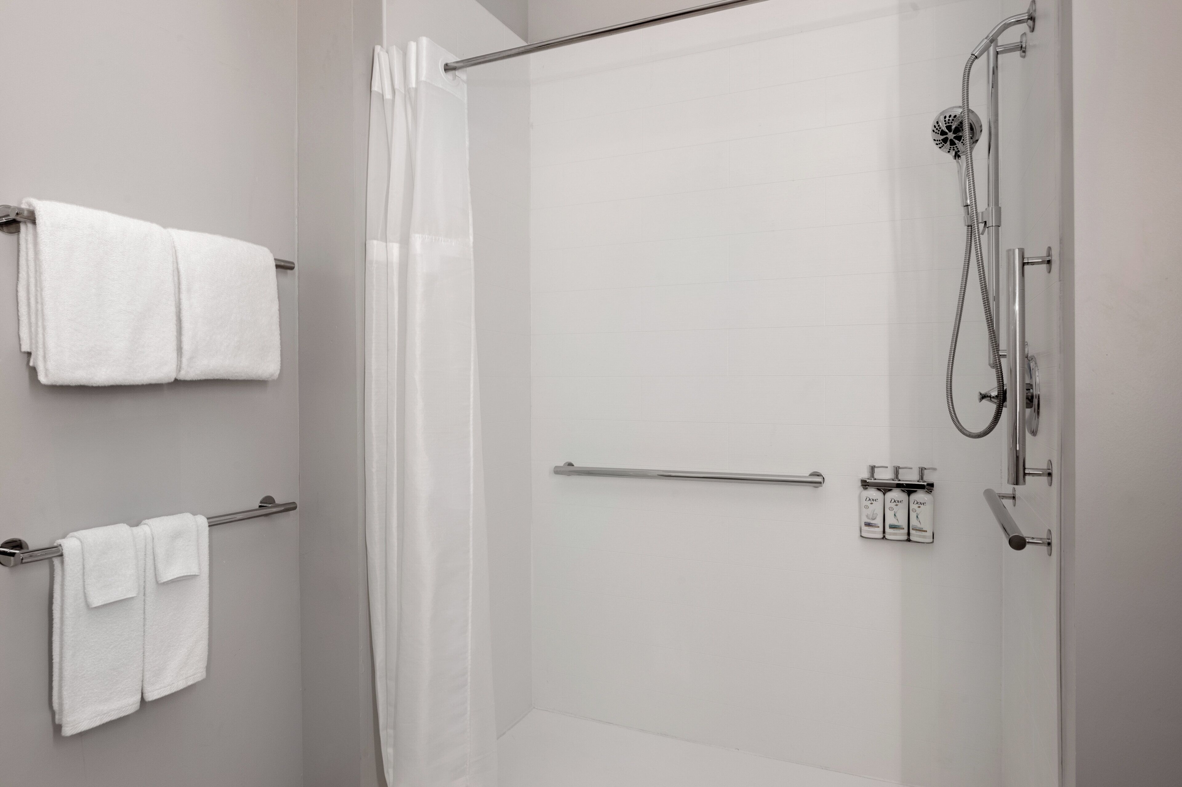 Área de chuveiro moderna com divisória de vidro, chuveiro manual e porta-toalhas com duas toalhas.