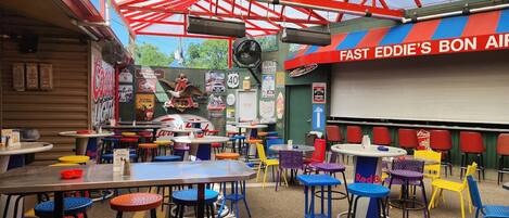 An outdoor dining area with colorful tables and chairs, a large mural, and a sign reading "FAST EDDIE'S BON AIR".