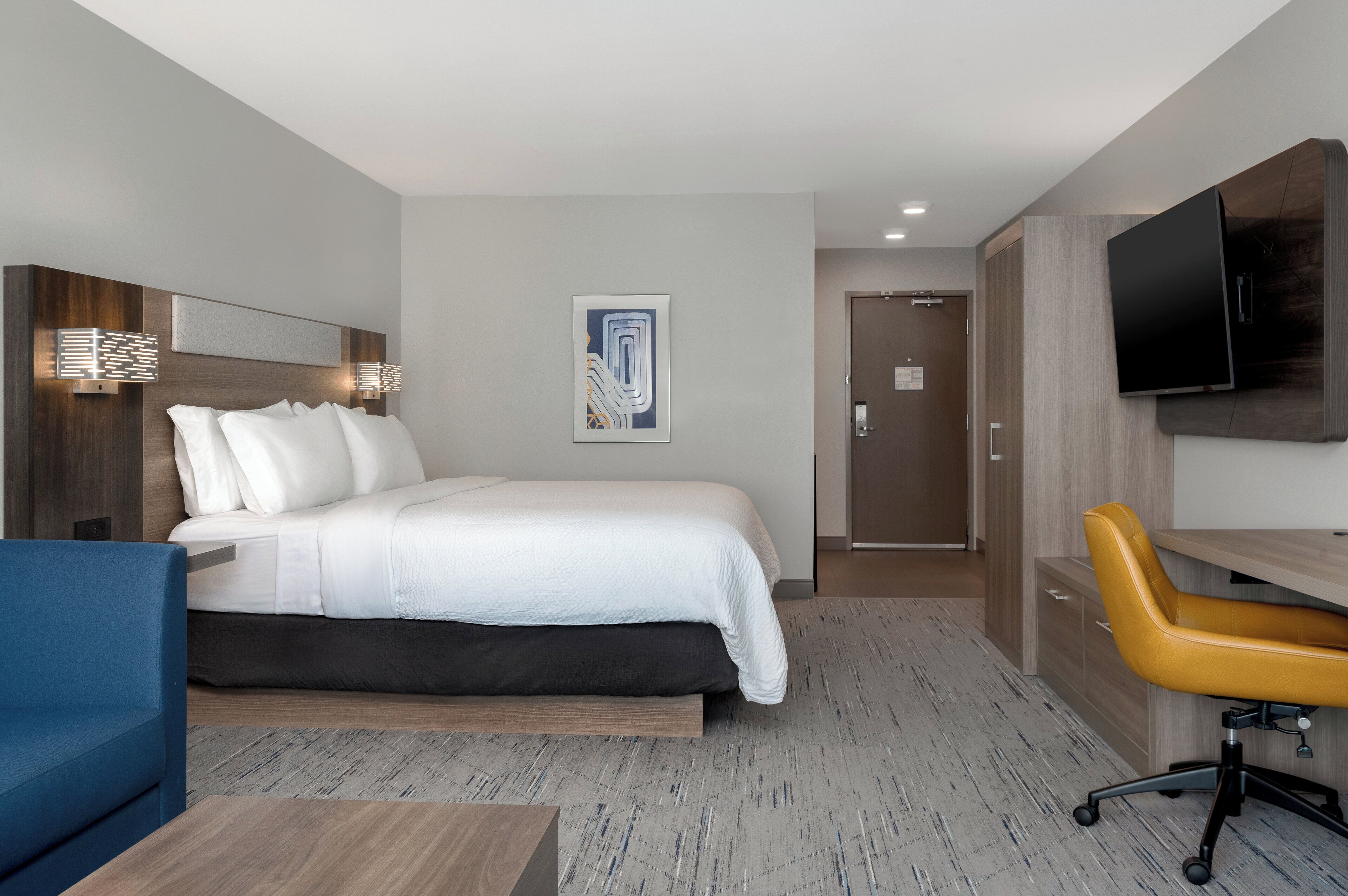 A hotel room with a bed, a desk, a chair, a television, and a door.