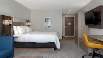 A hotel room with a bed, a desk, a chair, a television, and a door.