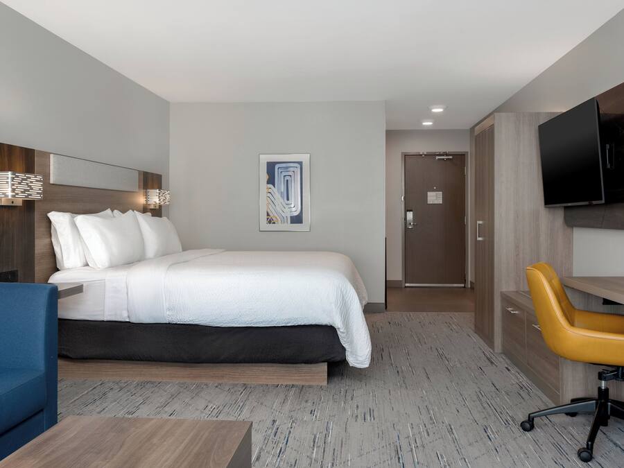 A hotel room with a bed, a desk, a chair, a television, and a door.