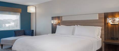 A modern hotel room with a large bed, a seating area, and a view of the cityscape.