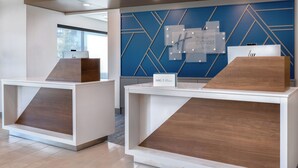 Two reception desks with a modern design, a blue geometric wall in the background, and a sign indicating the hotel name. - Holiday Inn Express and Suites Alton St Louis Area by IHG (Alton)