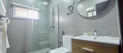 A modern bathroom with a glass shower enclosure, a toilet, a sink with toiletries, and a mirror.