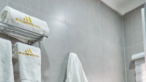 A bathroom with grey tiles, a towel rack with towels, and a robe hanging on the wall. - MUSADA LUXURY HOTELS AND SUITES (Abuja)