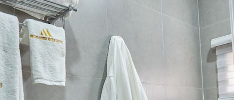 Un baño con baldosas grises, un perchero con toallas y una bata colgada en la pared.
