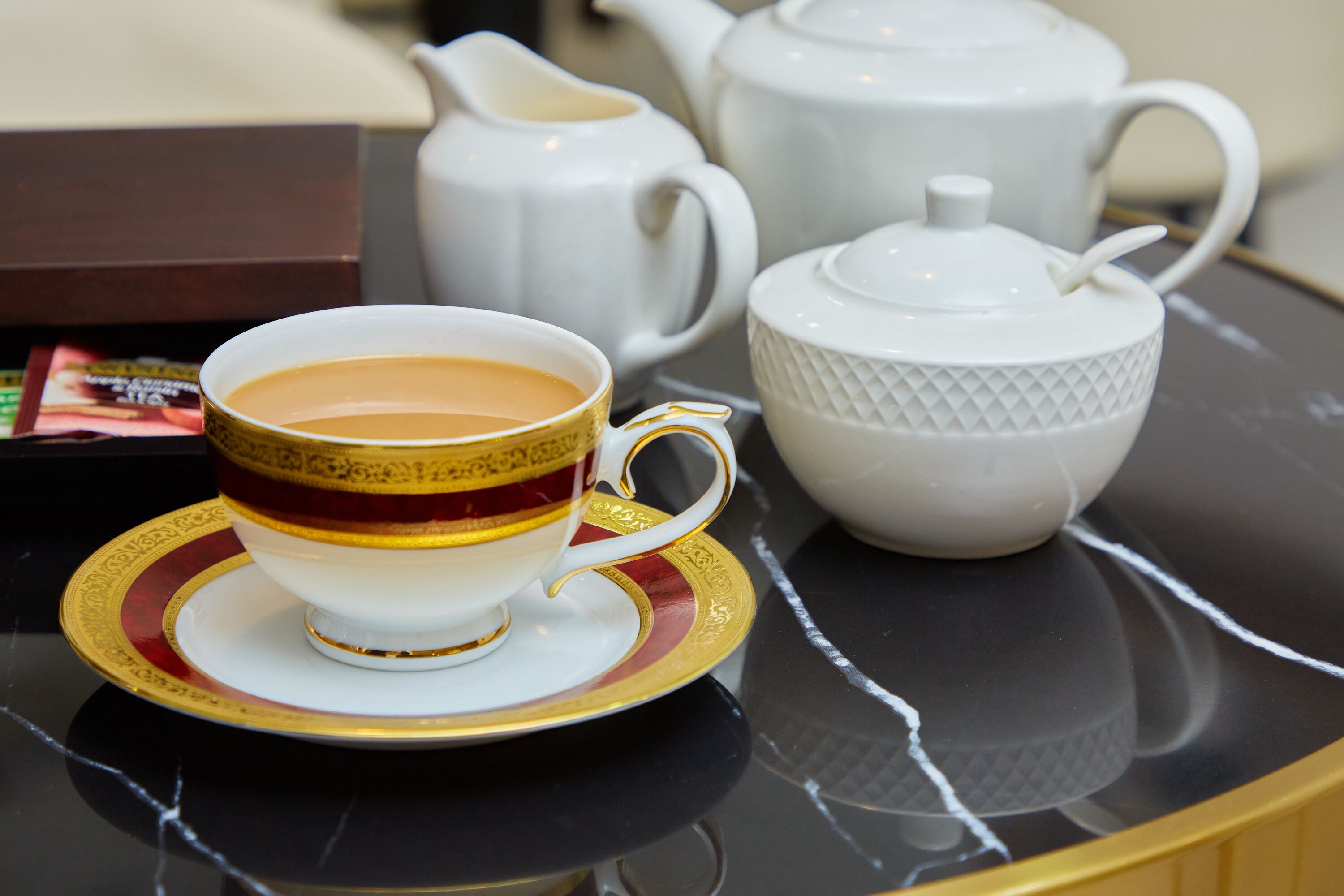 Un service à thé comprenant une tasse et une soucoupe, une théière et un sucrier, le tout posé sur une surface réfléchissante.