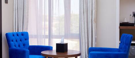 A hotel room with two blue armchairs, a small wooden table with a tissue box, and a bed.