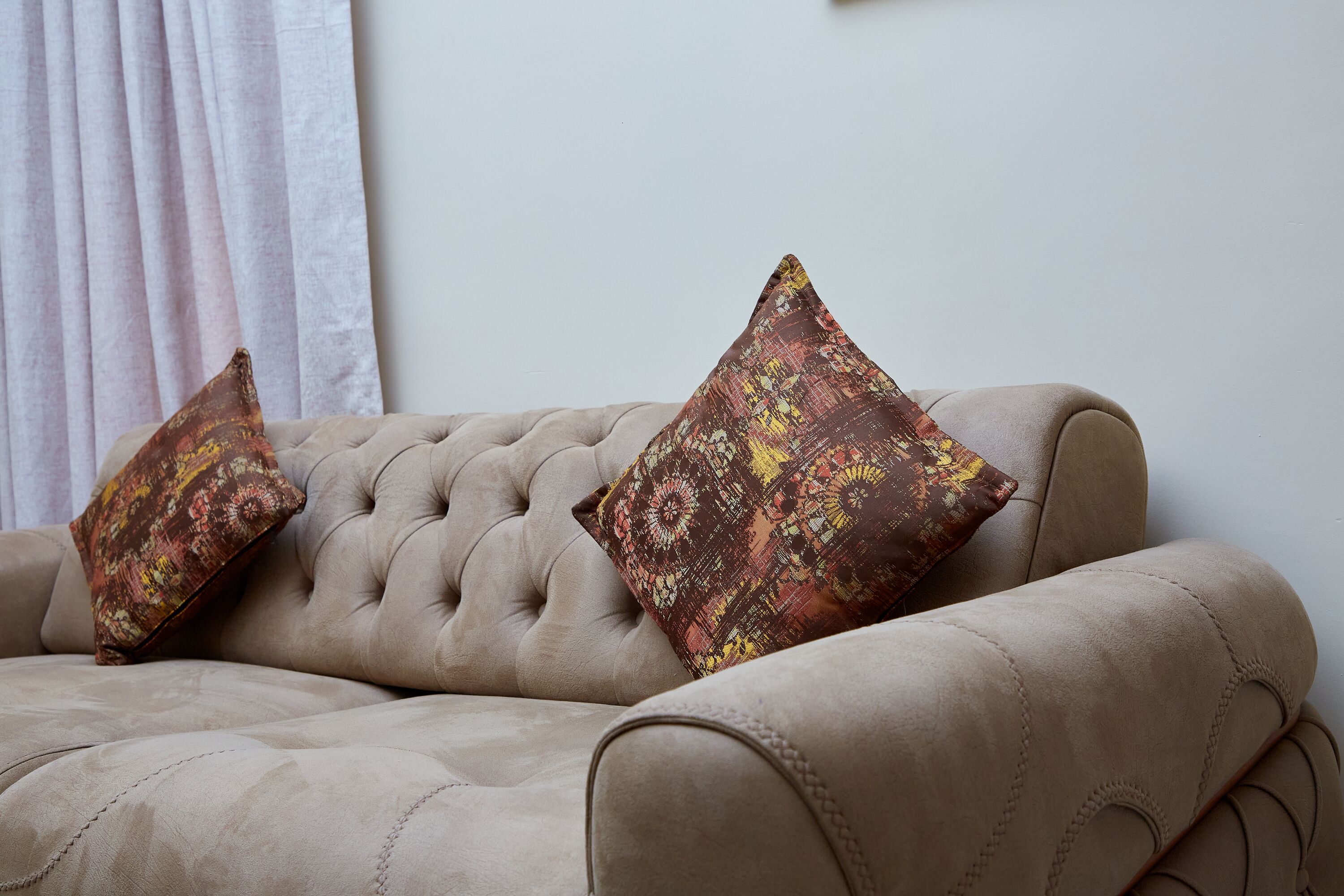 A tufted sofa with two patterned cushions.