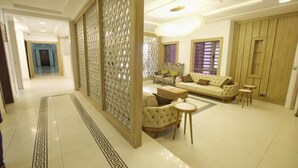 A spacious living area with a sofa, armchairs, and a coffee table. A decorative partition and a chandelier are also visible. - MUSADA LUXURY HOTELS AND SUITES (Abuja)