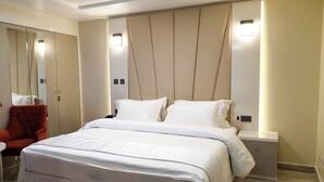 Camera d'hotel moderna con un letto grande, una poltrona rossa, un comodino e un armadio a muro con specchi.