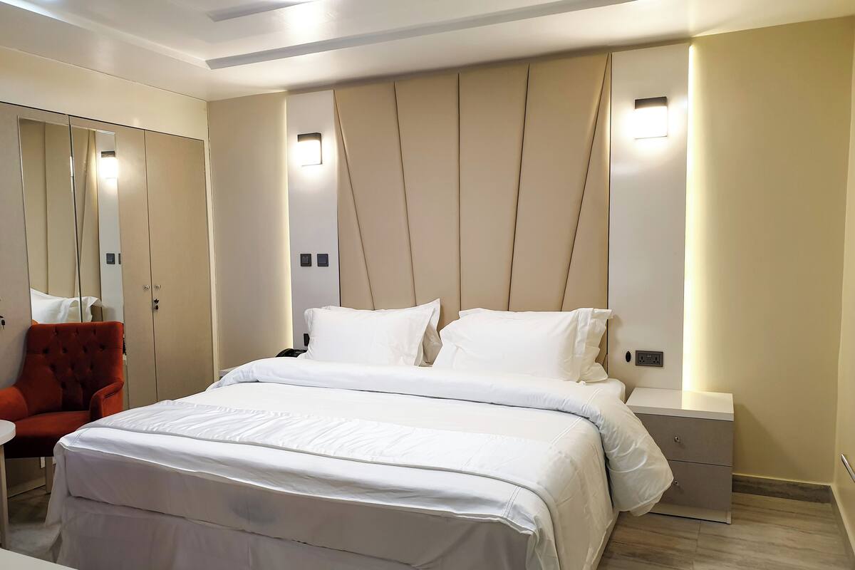 A modern hotel room with a large bed, a red armchair, a bedside table, and built-in wardrobe with mirrors.