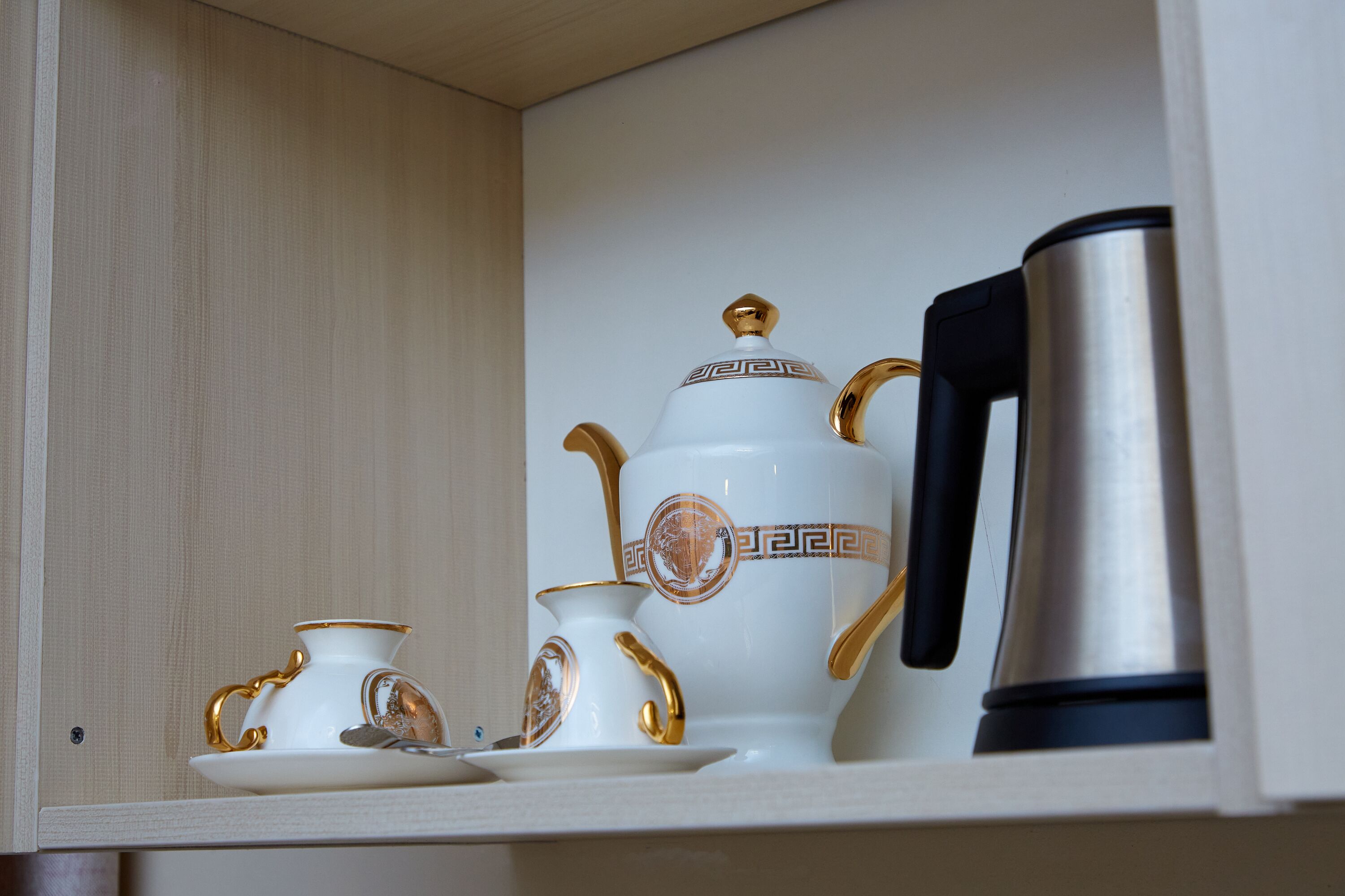 A tea set with a teapot, cups, and saucers in a cabinet.