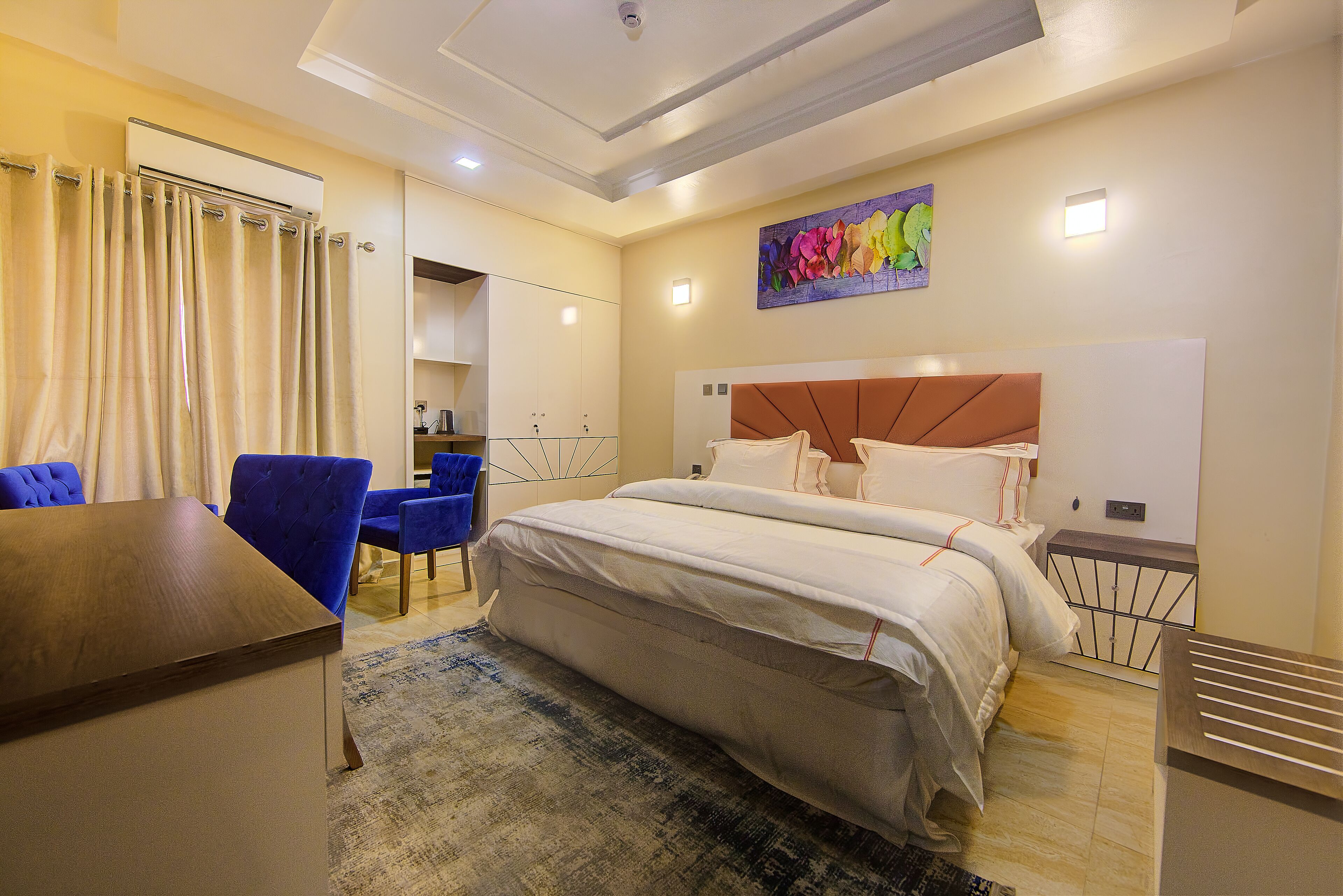 Une chambre d’hôtel avec un lit, un bureau et une chaise. Il y a un tableau au mur et une fenêtre avec des rideaux.