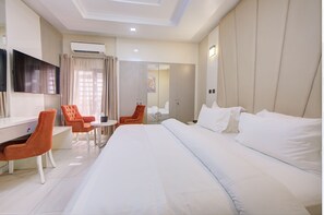 A hotel room with a large bed, a desk with a chair, a TV, and a wardrobe. - MUSADA LUXURY HOTELS AND SUITES (Abuja)