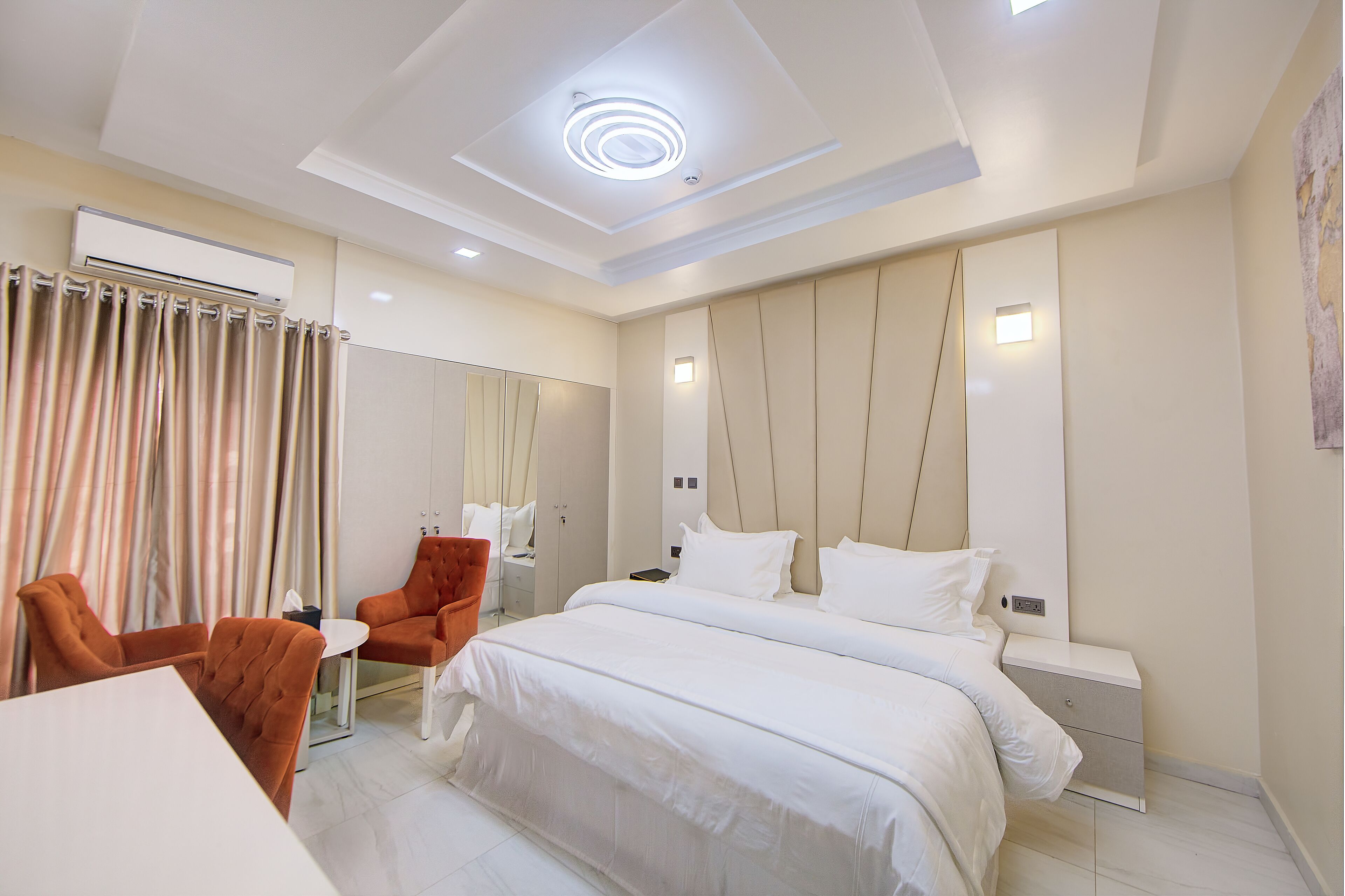 A modern hotel room with a large bed, a seating area with chairs, a small table, and a ceiling light.