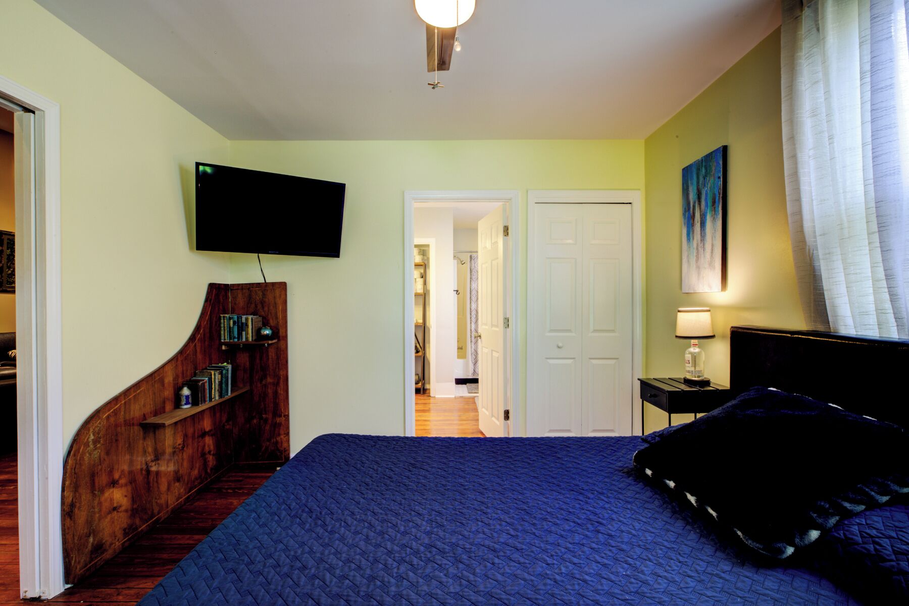 Ein Schlafzimmer mit einem großen Bett, einem an der Wand befestigten Fernseher, einer Holztreppe und einer Tür zu einem anderen Raum.