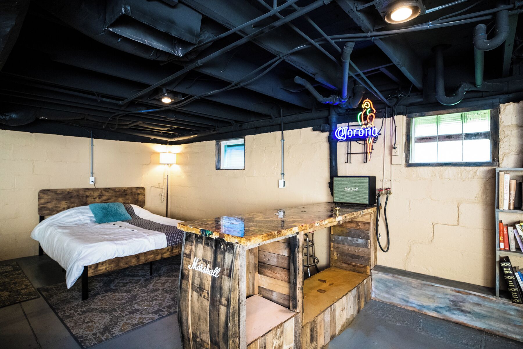 Una habitación con una cama, una barra de madera, un letrero de neón y una estantería.