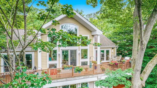 Une maison à deux étages dotée d’un balcon, de grandes fenêtres et d’une terrasse aménagée avec du mobilier d’extérieur.