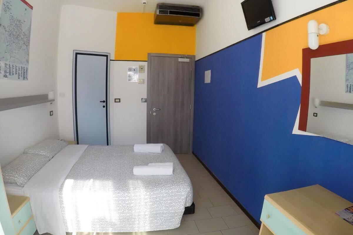 Une chambre d’hôtel équipée d’un lit, d’un bureau, d’une chaise, d’une armoire et d’un téléviseur fixé au mur.