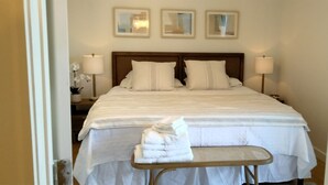 Une chambre d’hôtel avec un lit bien fait, deux lampes de chevet et une petite table sur laquelle sont pliées des serviettes.