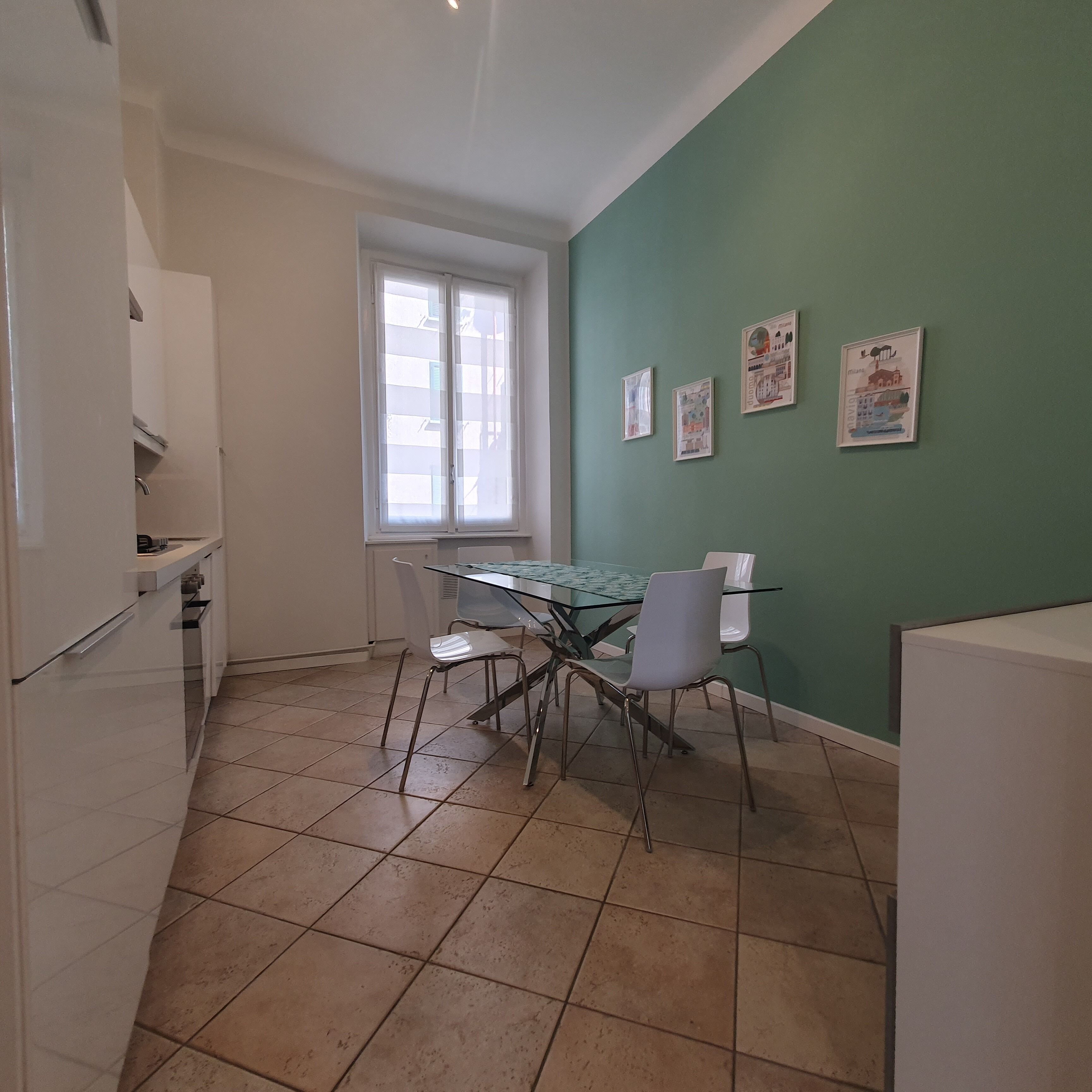 A small kitchen with a dining table and chairs, a window, and a green wall with framed pictures.
