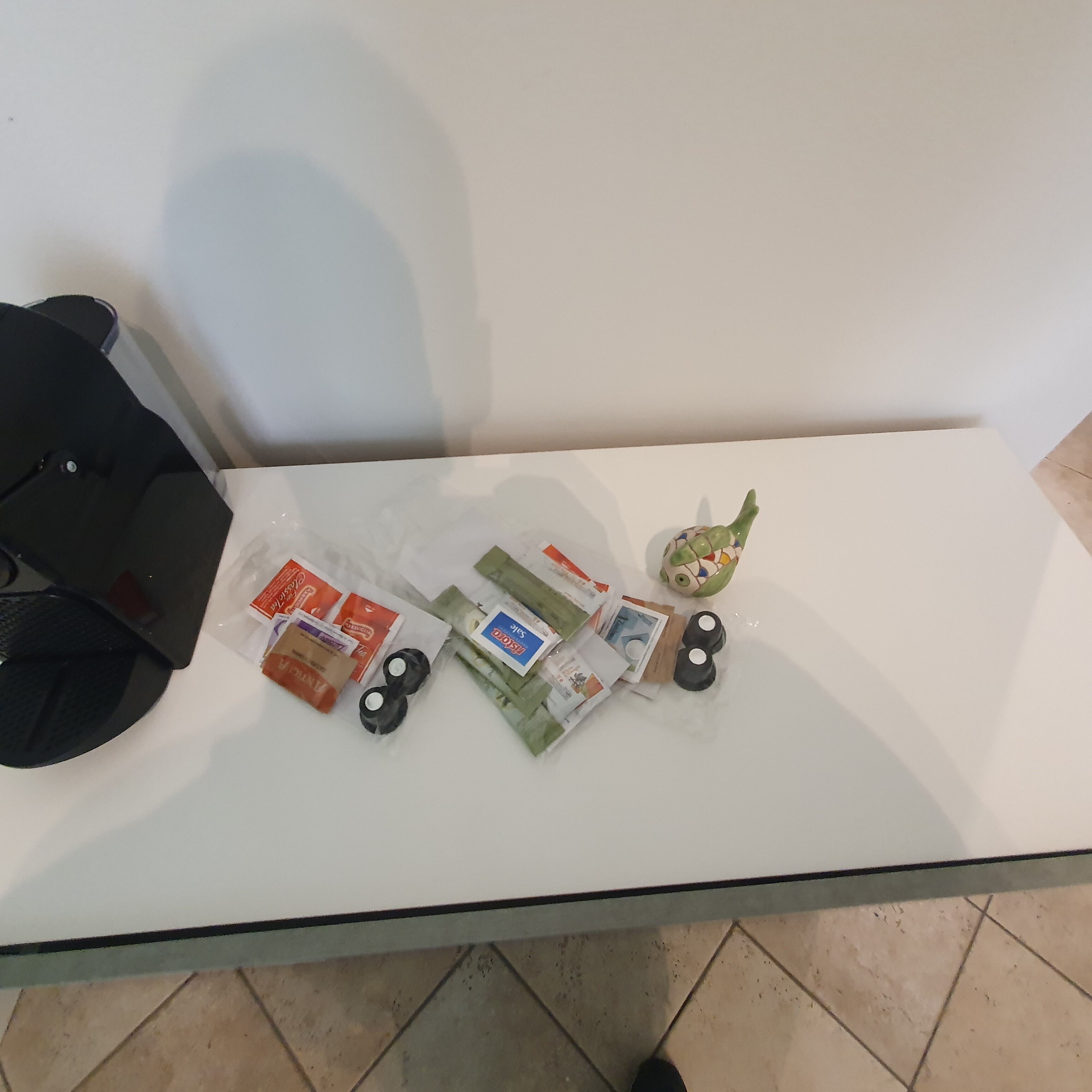 Una mesa con cubierta de vidrio y varios objetos, incluyendo un bolso negro, varios paquetes y una figurita decorativa de rana.