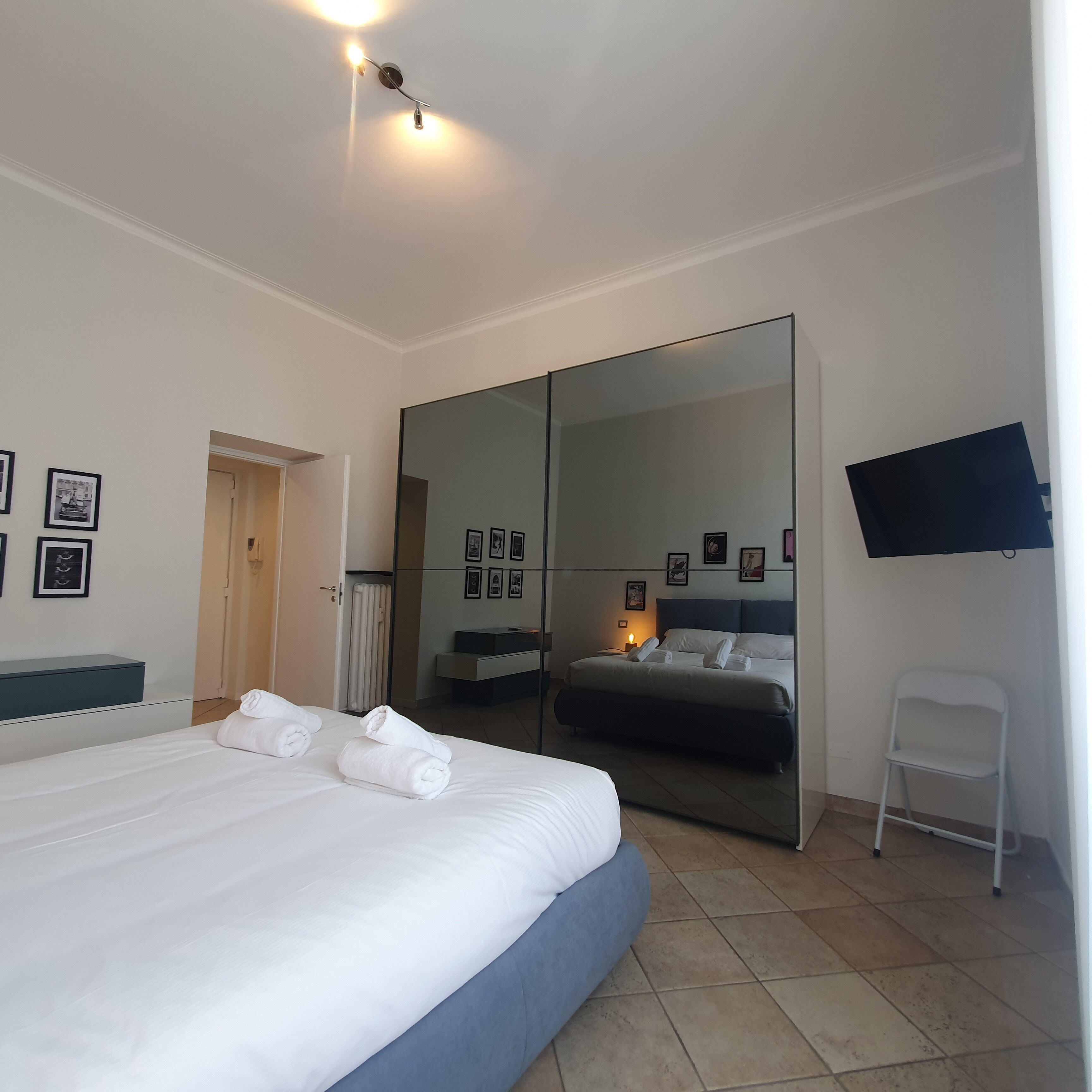 A hotel room with a large bed, a wardrobe, a mirror, a TV, and a chair.