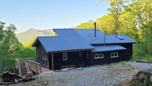 Eine schwarze Holzhütte mit Metalldach, Schornstein und einer Terrasse mit Treppe zum Eingang.