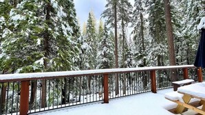 A snow-covered deck with a wooden railing, surrounded by tall evergreen trees. - Pinecrest Escape (Cold Springs)