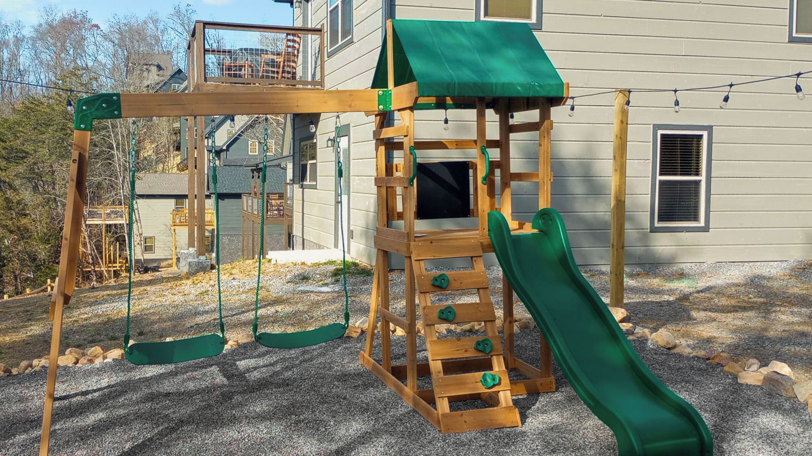 A wooden play structure with a slide and climbing elements in front of a house.
