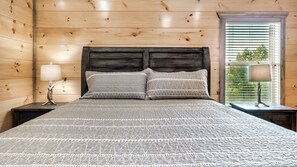 Una habitación con paneles de madera, una cama, dos mesitas de noche y un ventanal con persianas.