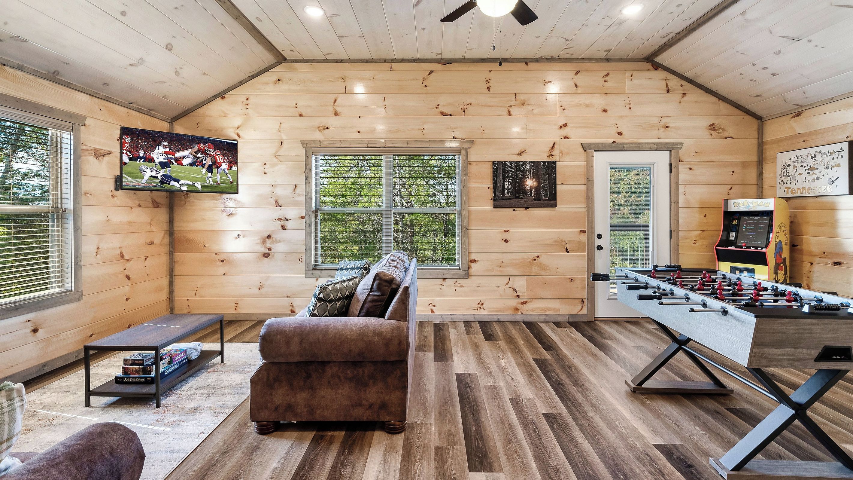 Un interior acogedor de madera con un sofá, mesa de futbolín y televisor montado en la pared.
