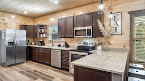 A modern kitchen with wooden cabinetry, stainless steel appliances, and granite countertops. - Cabin Bliss | Hot Tub, Games & Scenic Yard Escape (Sevierville)