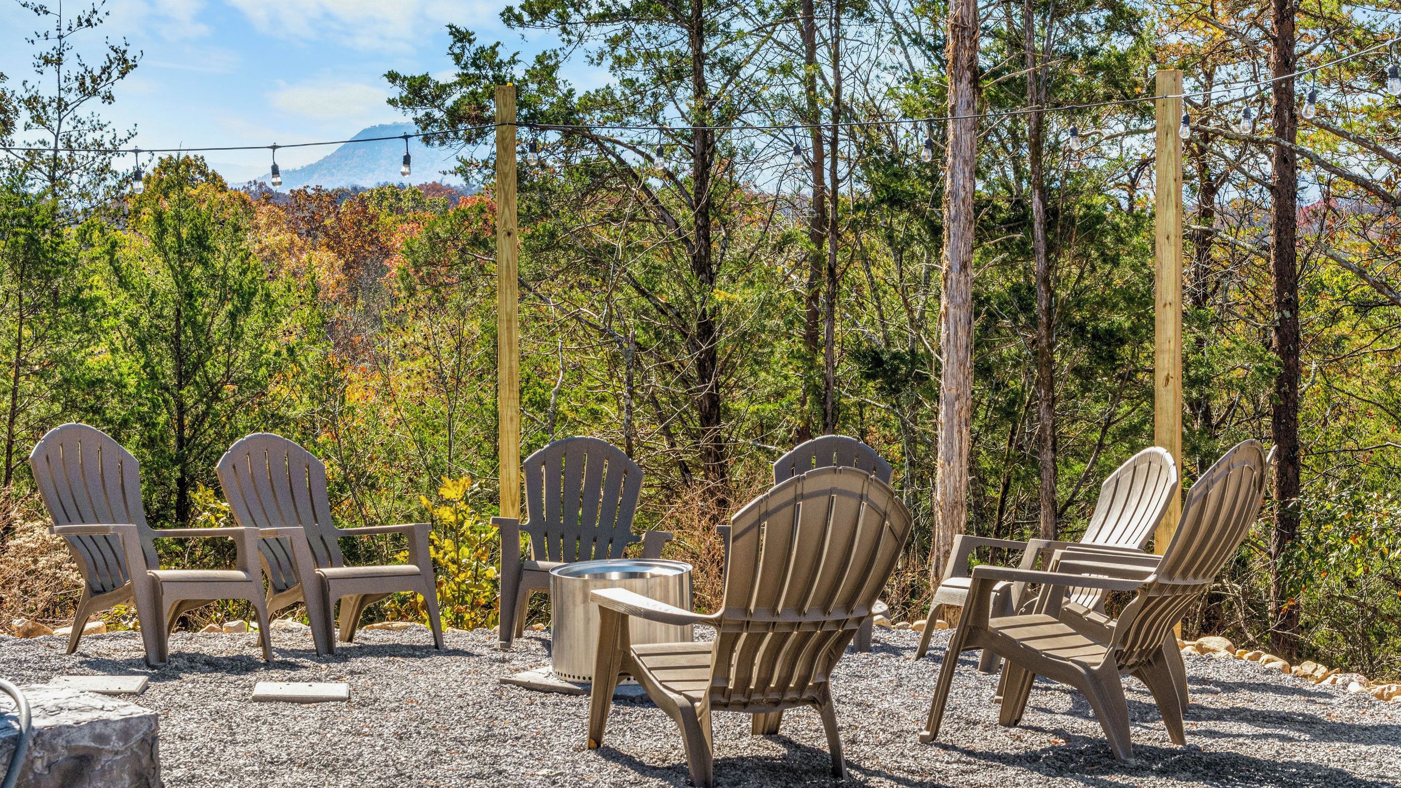 Outdoor seating with Adirondack chairs and a metal table, surrounded by gravel and trees.