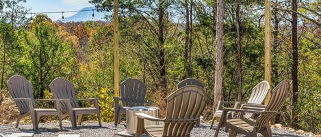 Outdoor seating with Adirondack chairs and a metal table, surrounded by gravel and trees.