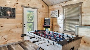 Una habitación con mesa de fútbol de mesa, máquina de videojuegos Pac-Man y una puerta que da al exterior.