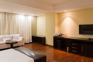 A hotel room with a sofa, a small table, a coffee table, a TV, and a minibar.