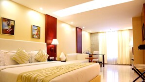 A hotel room with a large bed, a desk, a chair, and a window with curtains. - Trinity Grand (Raigarh)