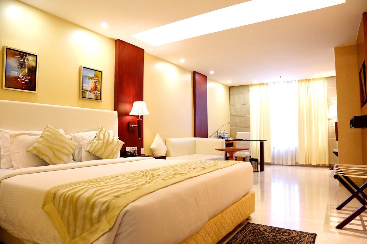 Habitación de hotel con una cama grande, un escritorio, una silla y un ventanal con cortinas.