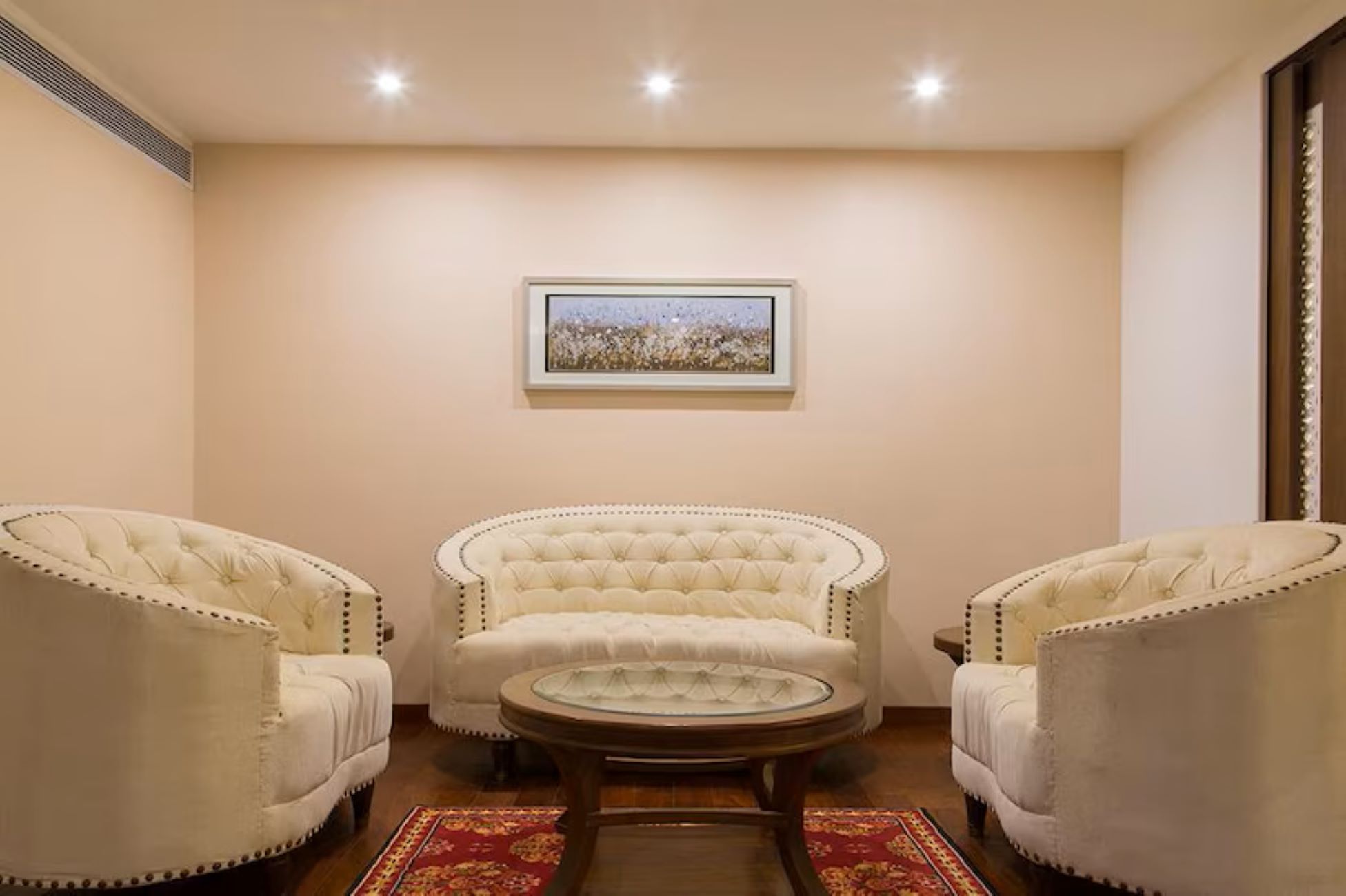 A room with three upholstered chairs, a round table, and a framed picture on the wall.