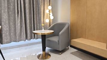 Una habitación moderna con un sillón gris, una mesa redonda con un florero y flores, y una lámpara de pared.