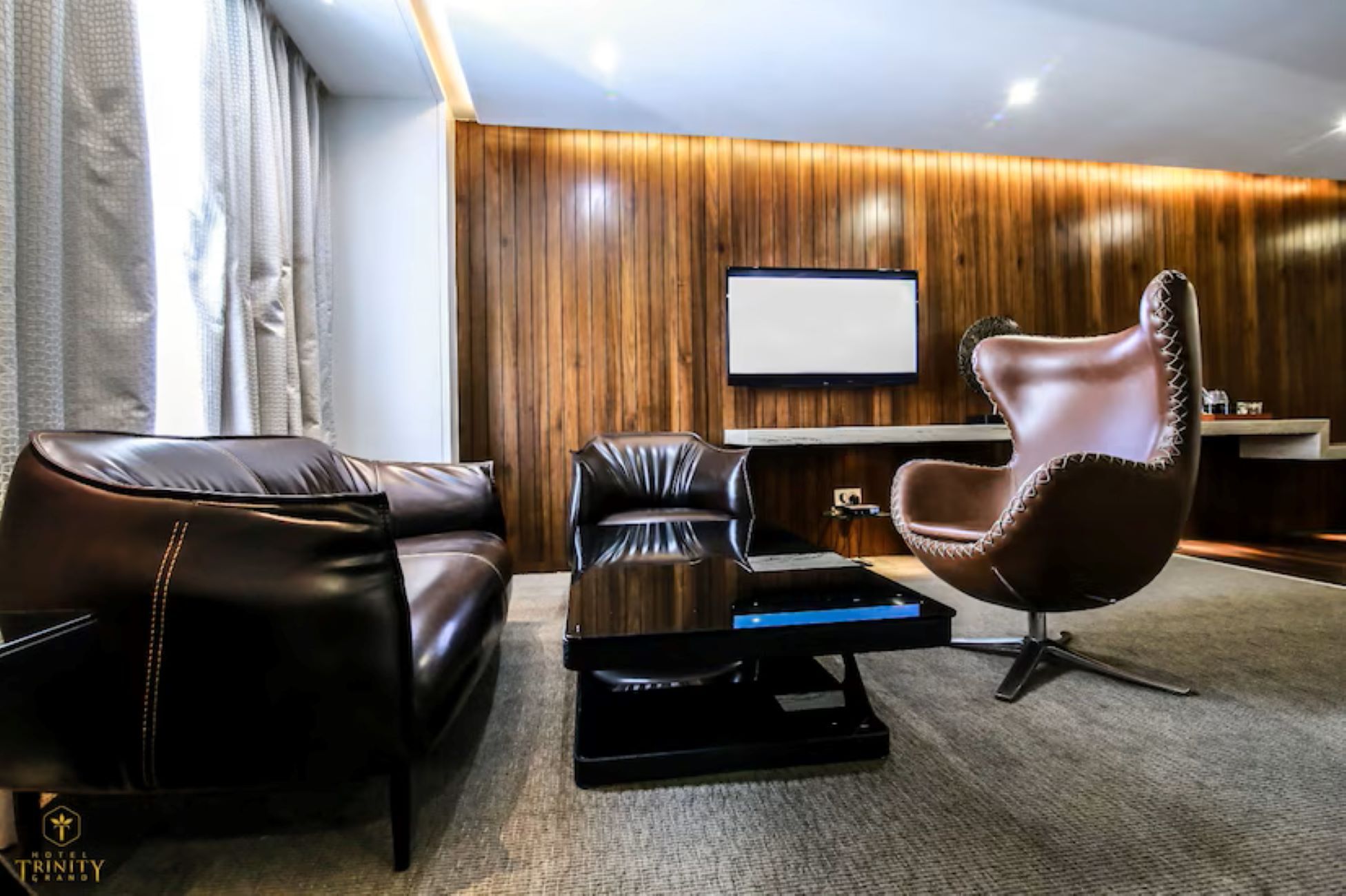 A modern living room with leather sofas, a unique chair, a flat-screen TV, and a wooden wall.